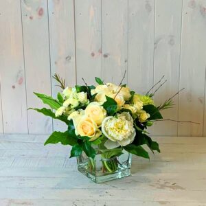 flower arrangement in creams greens and whites in glass cube vase.Creams